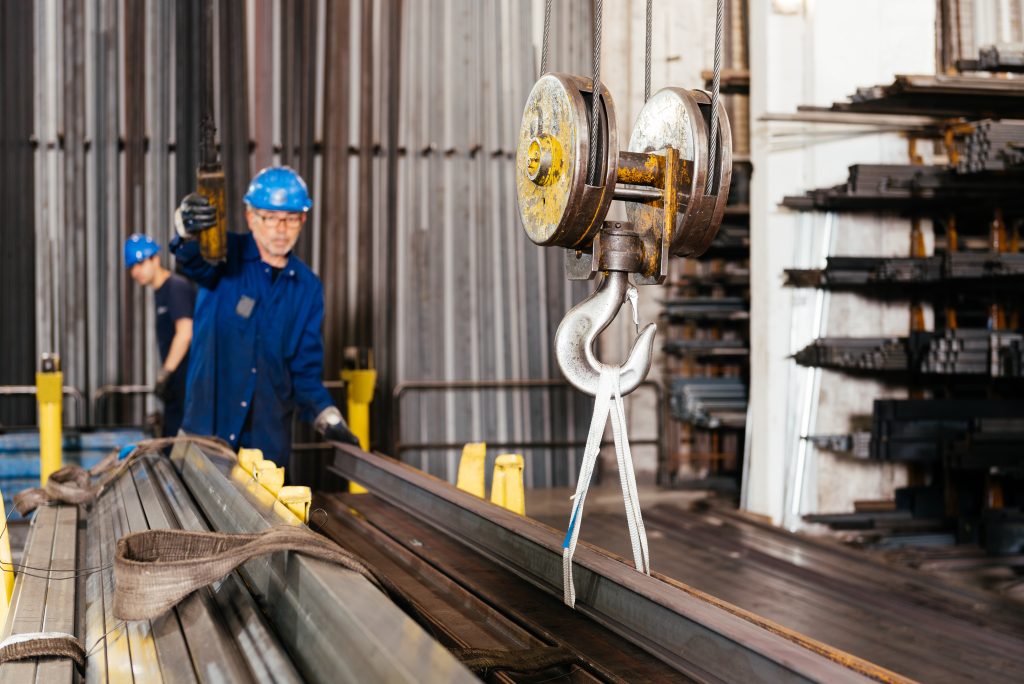 Male worker in protective helmet and gloves standing near crane and working in professional metal store